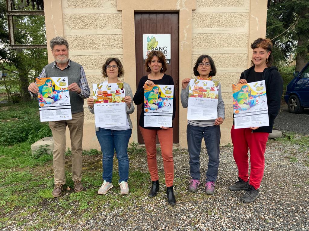 Membres de la comissió organitzadora de la Fira de la Llavor, amb la regidora de Promoció Econòmica, Núria Arrebola, davant del Banc de Llavors. Mostren els cartells de la fira i del concurs de conserves.