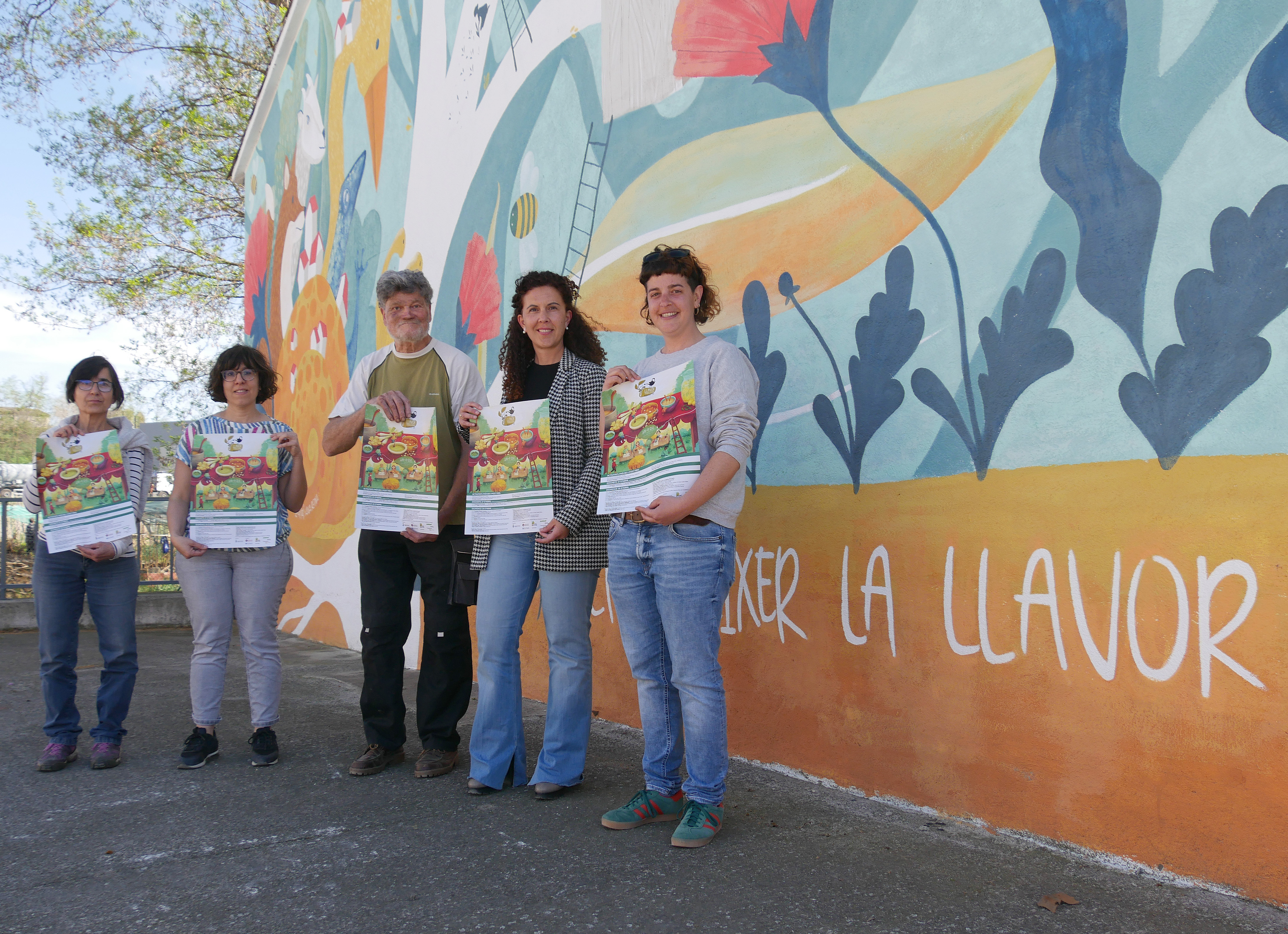 Membres de la comissió organitzadora de la Fira de la Llavor, amb la regidora de Promoció Econòmica, Griselda Arrey, davant el mural de la fira que es va pintar per celebrar la 10a edició.